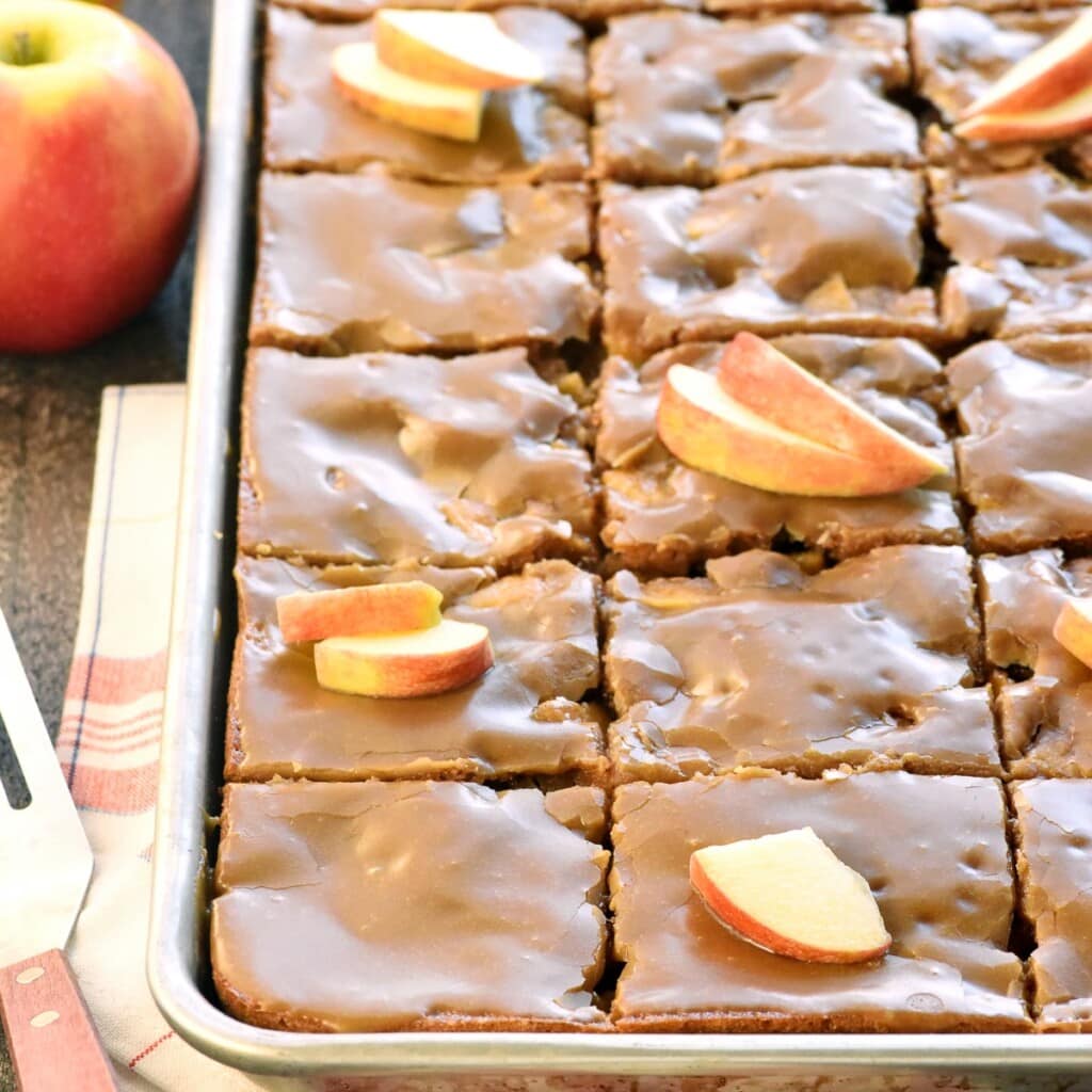 Caramel Apple Cake sliced in pan with caramel glaze and apple garnish.