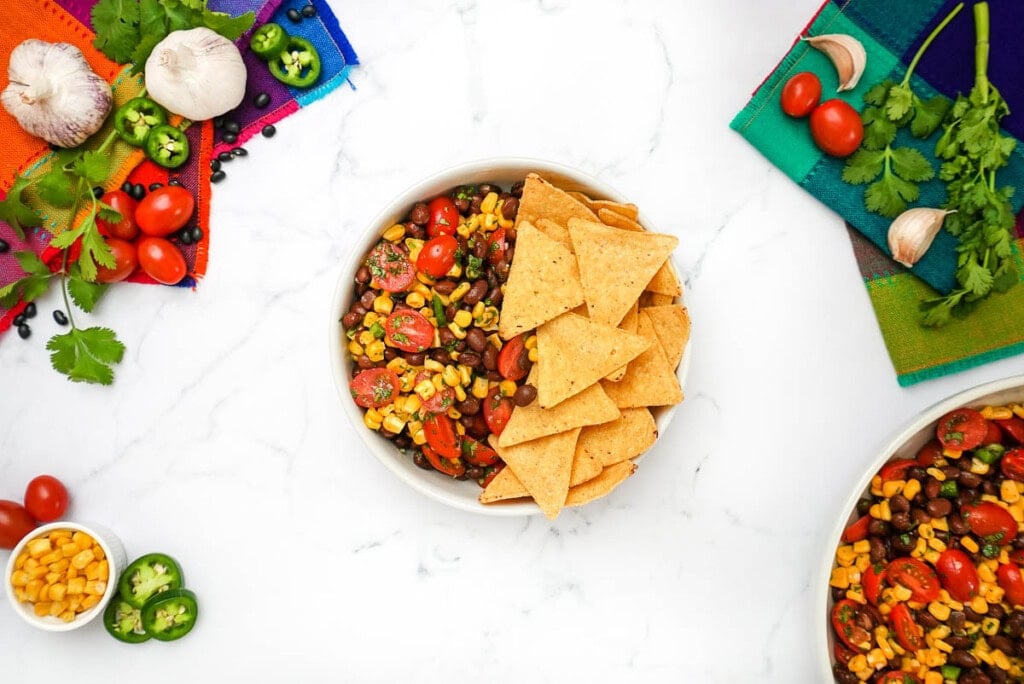 Black Bean and Corn Salsa with tortilla chips and ingredients on table.