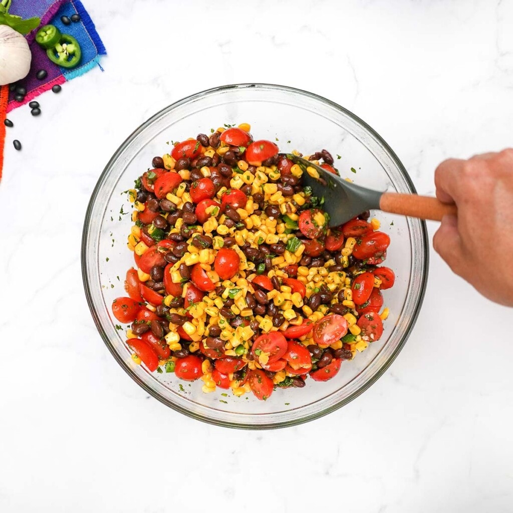 Mixing corn black bean salad in glass bowl.