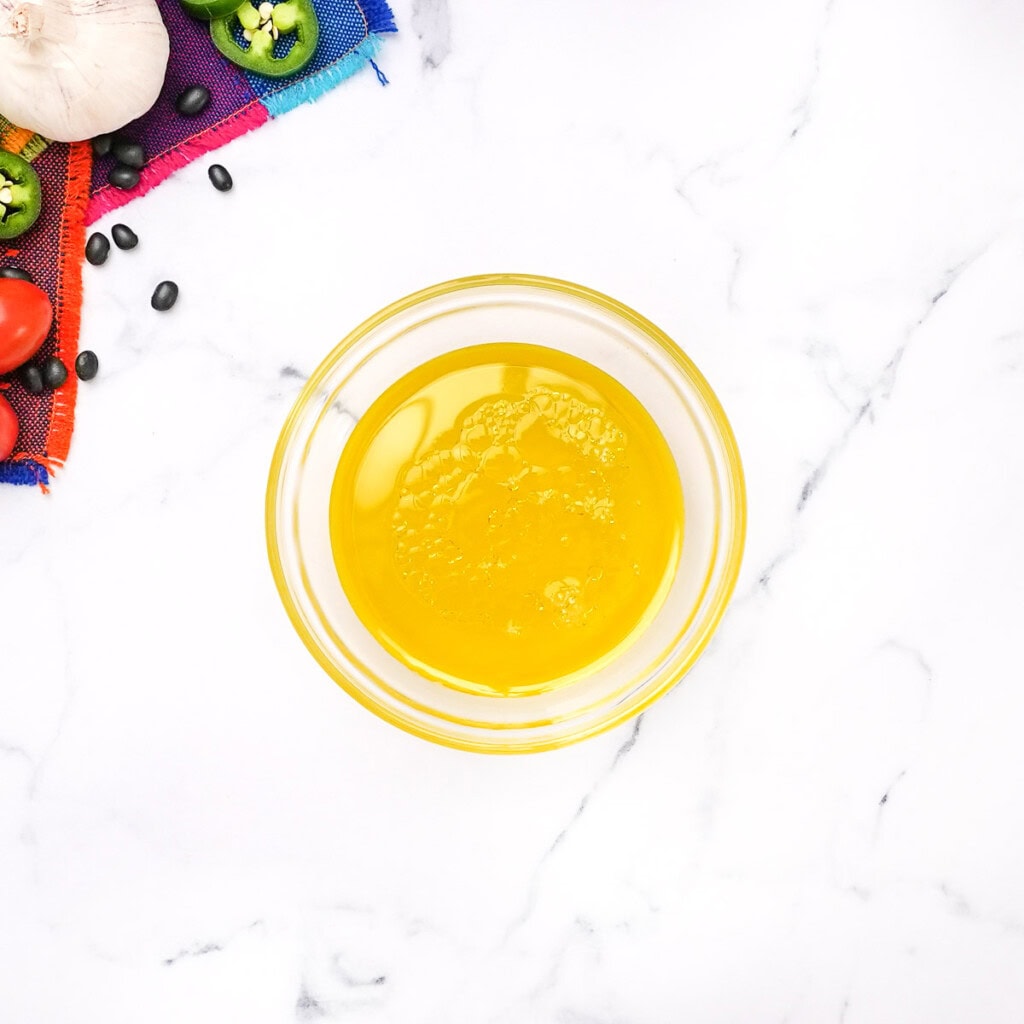 Adding oil and lime juice to bowl for vinaigrette to top corn and black bean salad.