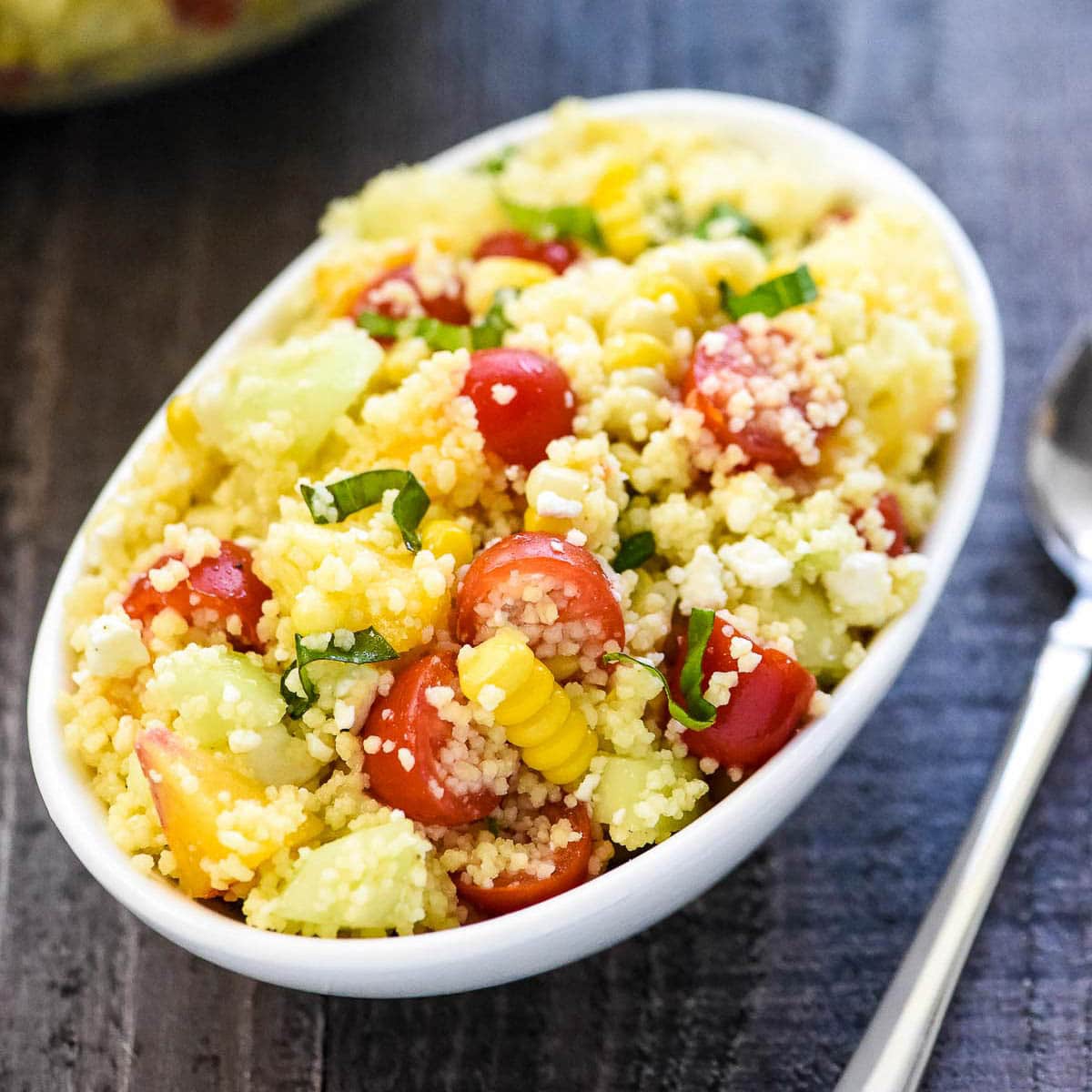 Couscous Salad in white bowl with spoon on table.
