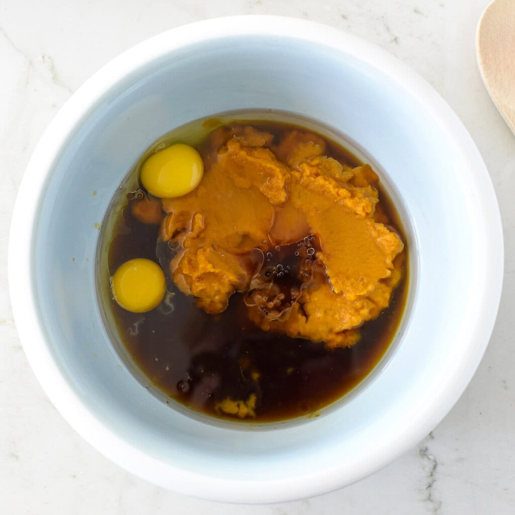 Pumpkin, maple syrup, coconut oil, eggs, and vanilla in bowl.