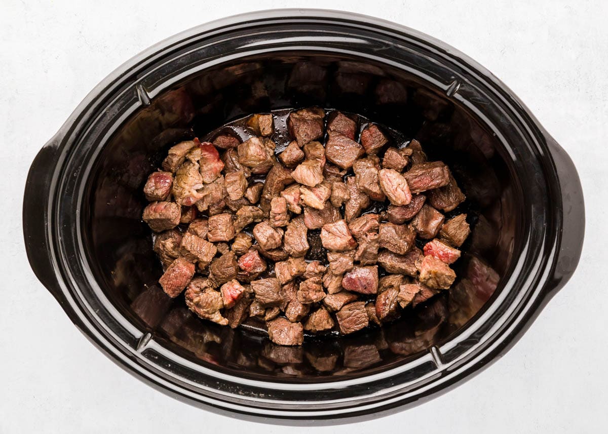 Seared chunks of beef transferred to slow cooker.