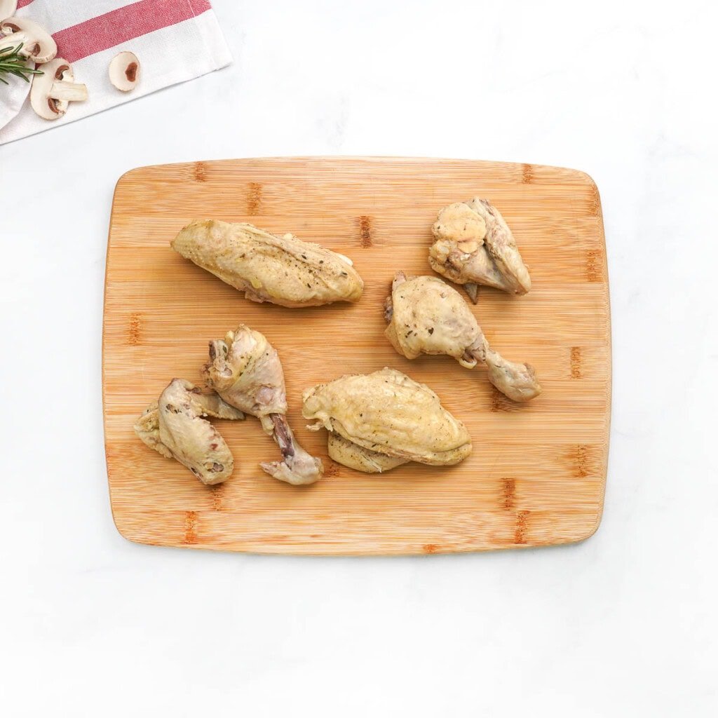 Cooked chicken pieces on cutting board.