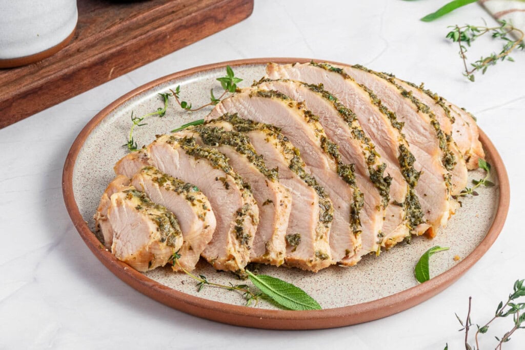 Slow Cooker Turkey Breast sliced on plate with herbs.