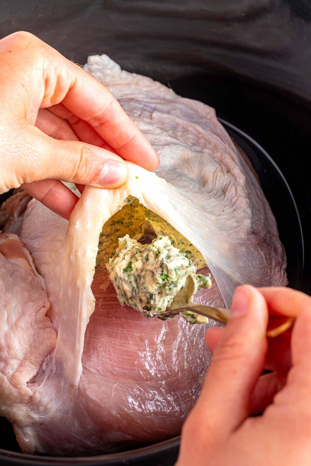 Slipping herb butter under skin of turkey breast in slow cooker.