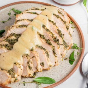 Crockpot Turkey Breast sliced on platter with herbs and gravy.