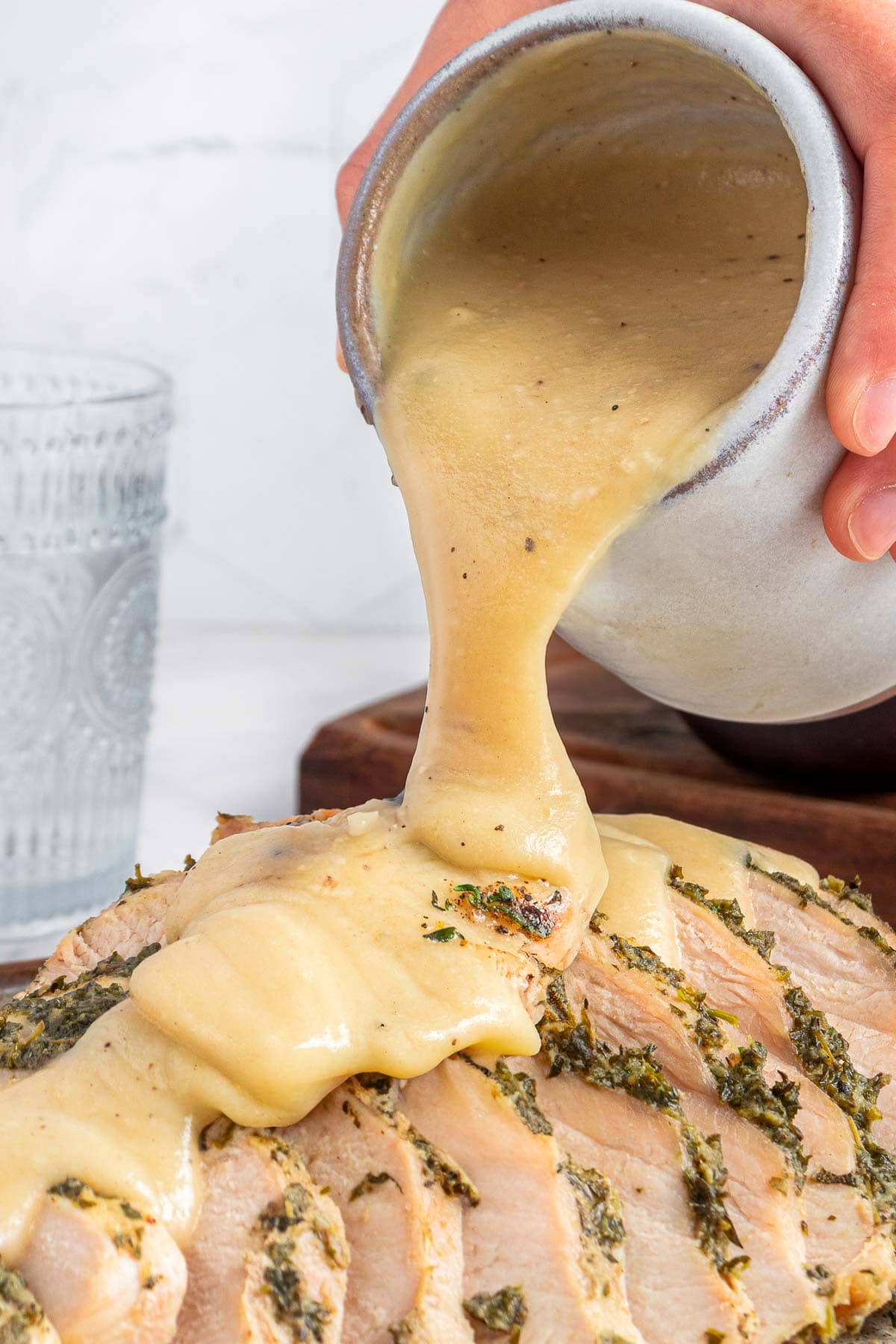 Pouring homemade turkey gravy over sliced turkey on platter.