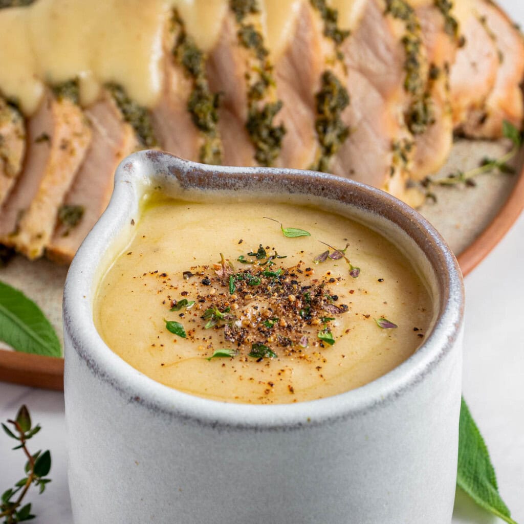 Make Ahead Turkey Gravy in jug and over sliced turkey with herbs.