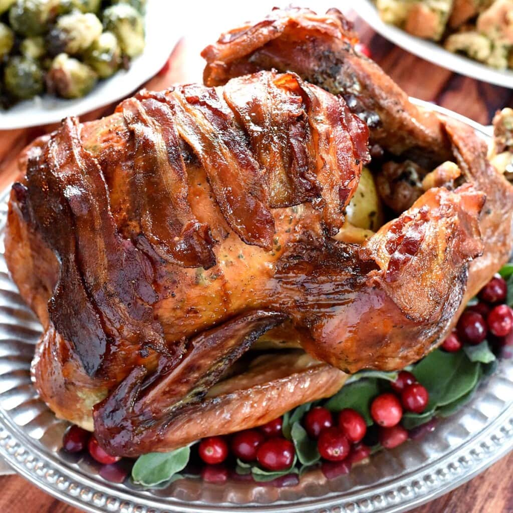 Maple-Glazed Turkey with Bacon with sage leaves and fresh cranberries garnishing platter.