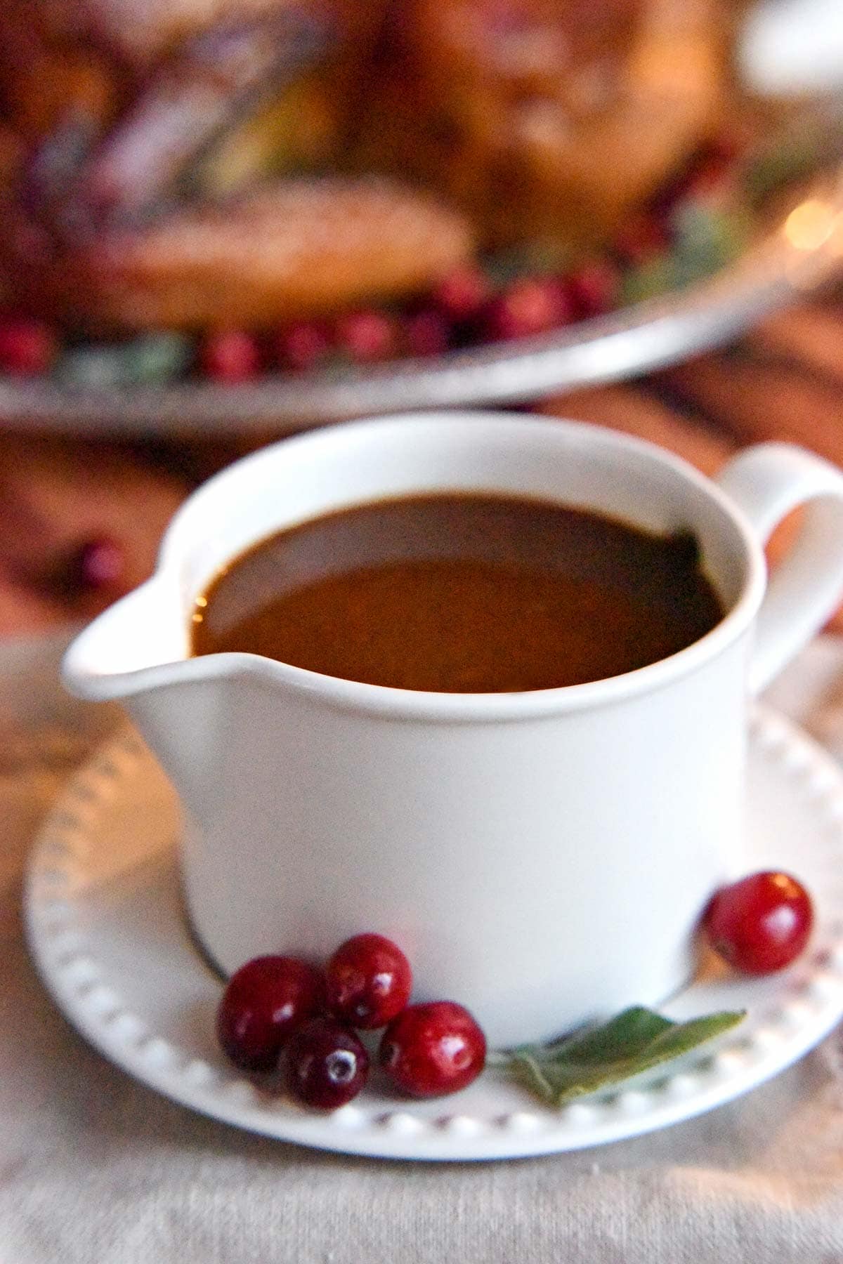 Gravy in gravy boat with sage and fresh cranberries on the side.