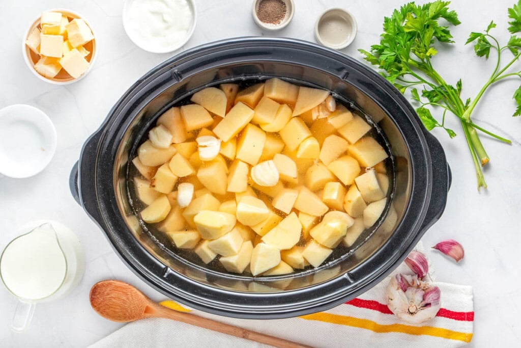 Potato chunks and smashed garlic cloves in slow cooker.