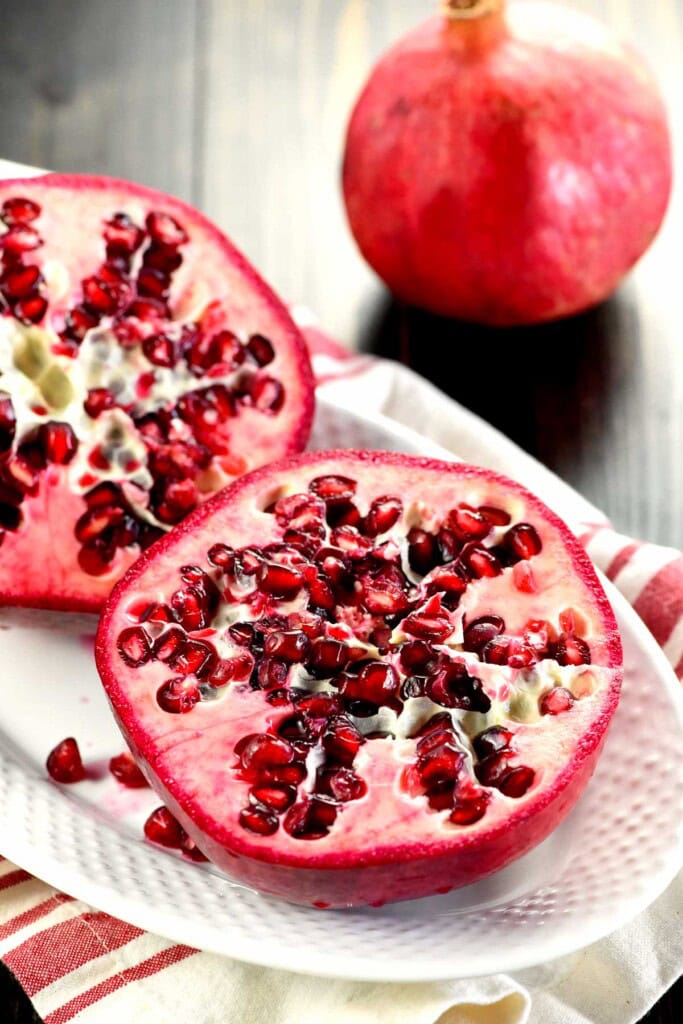 Pomegranate cut in half with another on table.