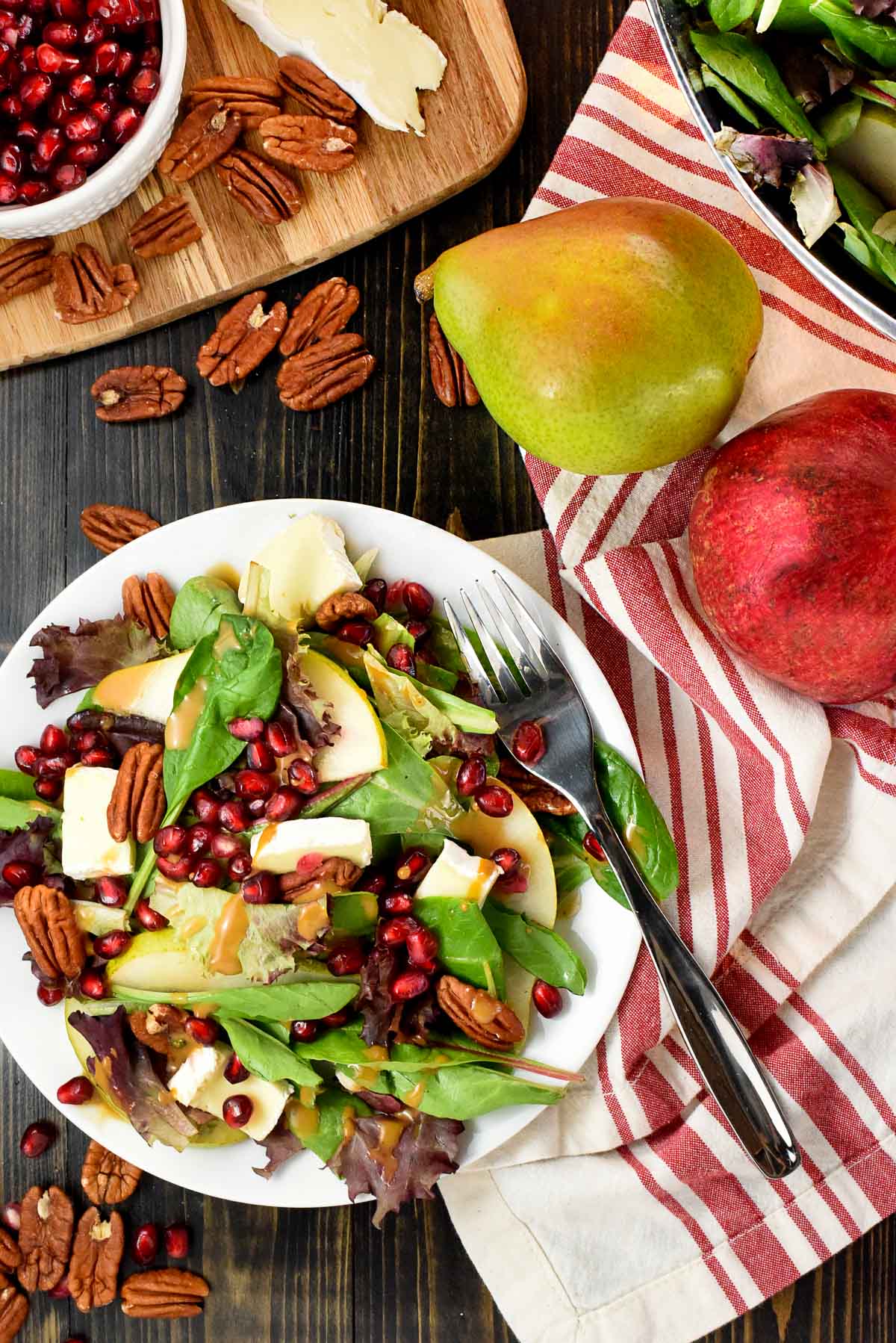 Thanksgiving Salad surrounded by ingredients to make it including pomegranate, pear, brie, and pecans.