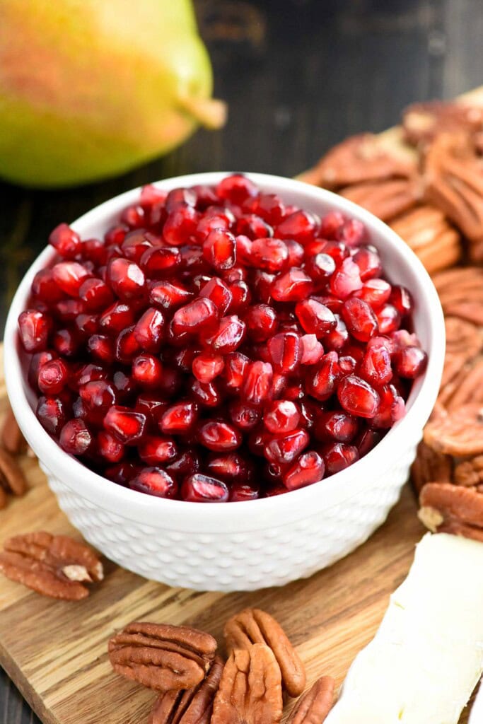 Bowl of pomegranate arils surrounded by toasted pecans.