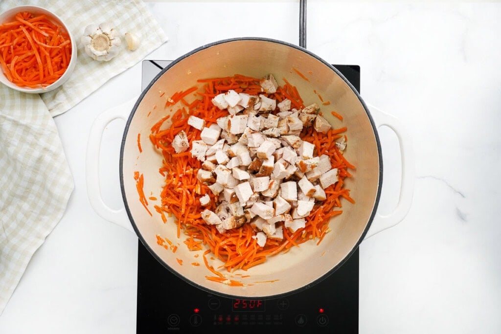 Adding diced chicken to sauteed carrots in pot.