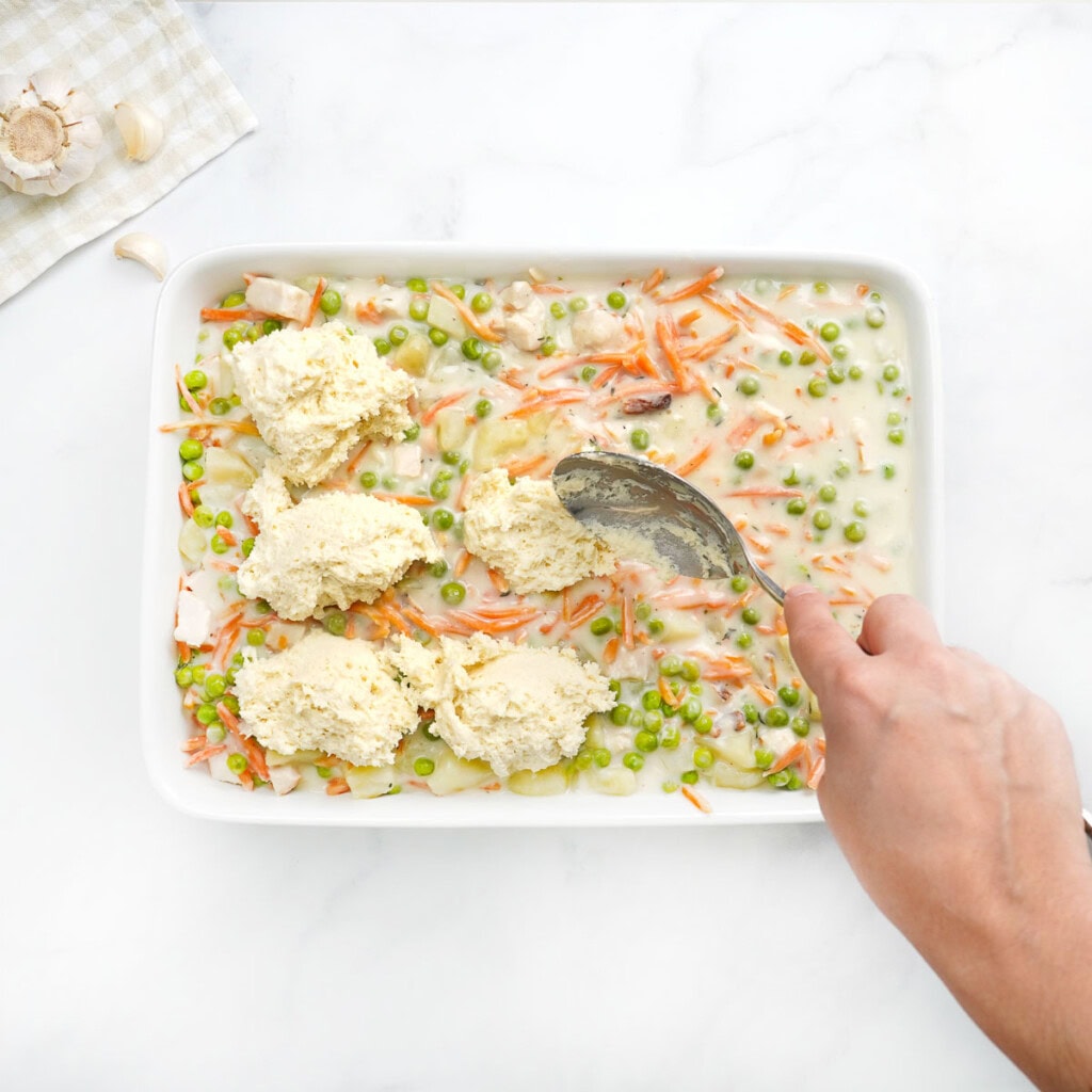 Adding biscuit dough on top of Chicken Pot Pie Casserole filling in dish.