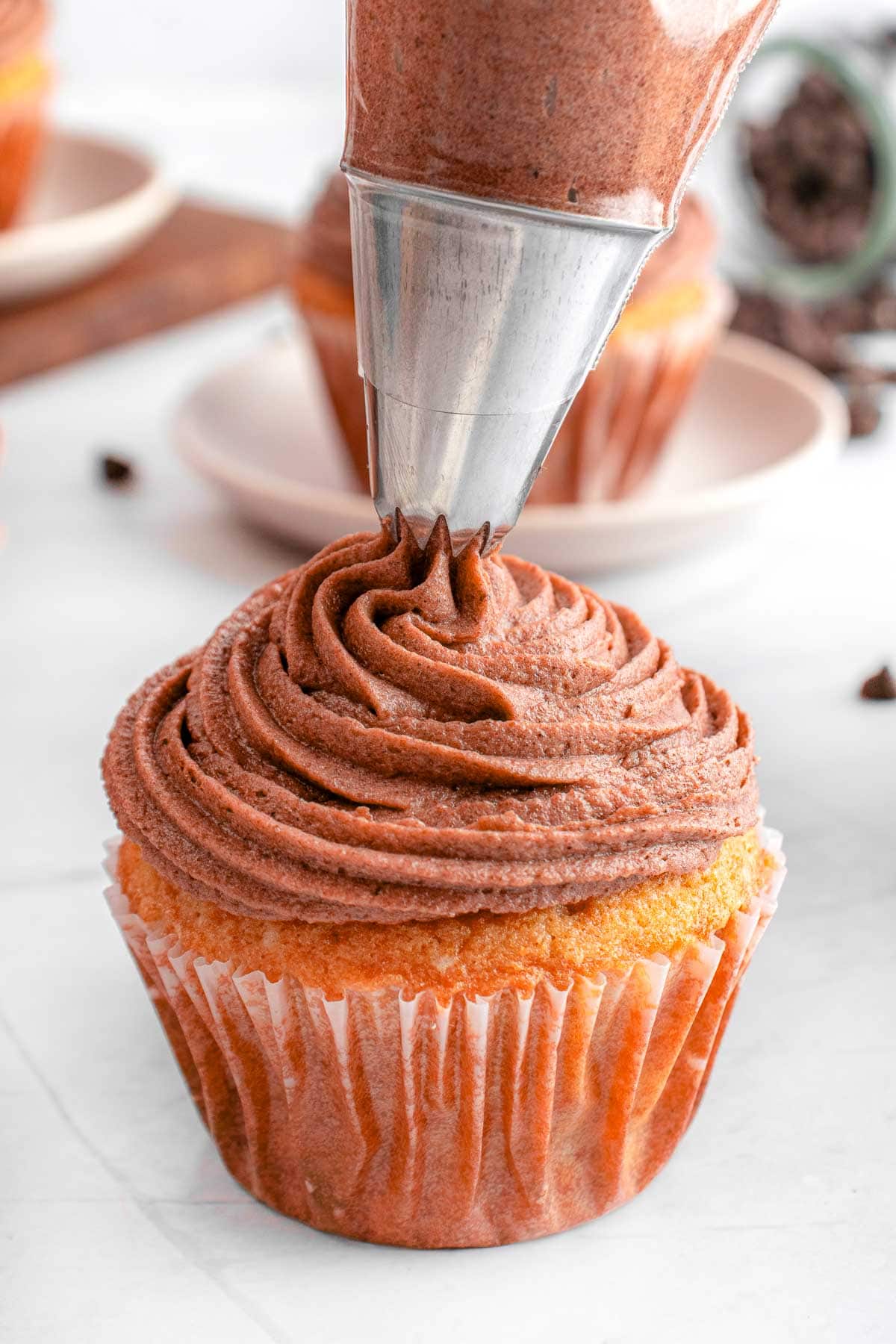 Piping cream cheese chocolate frosting onto a cupcake.