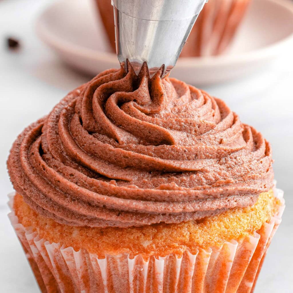 Chocolate Cream Cheese Frosting being piped onto yellow cupcake.