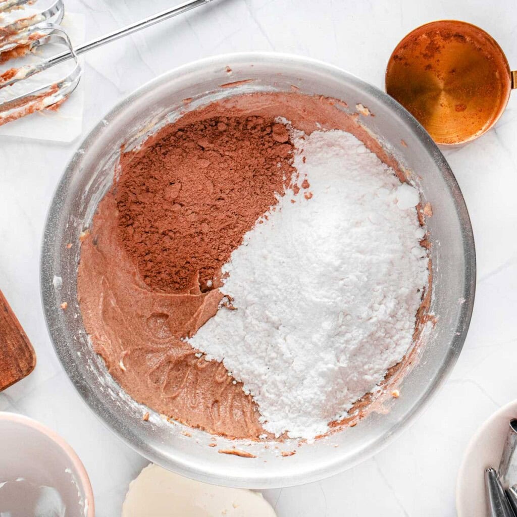 Adding final portions of powdered sugar and cocoa powder to bowl.