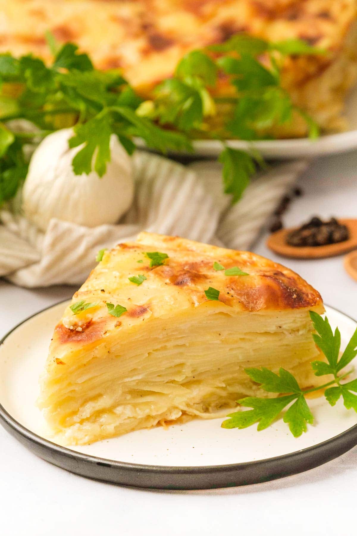 Gruyere Scalloped Potatoes wedge on plate with serving dish in background.