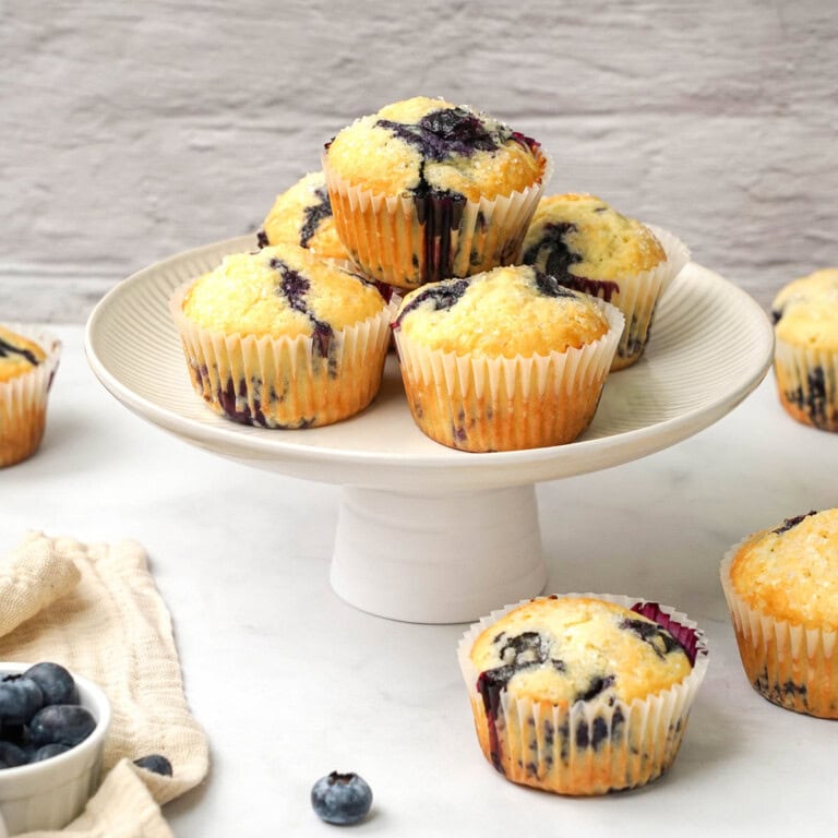 Easy Blueberry Muffins stacked on platter and scattered across table with extra blueberries.