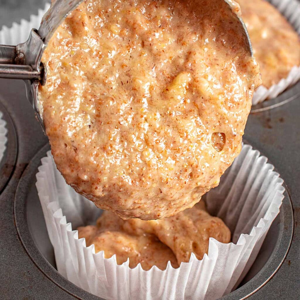 Scooping banana muffins healthy batter in muffin pan.