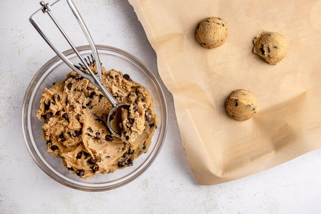 Scooping best Brown Butter Chocolate Chip Cookies dough onto lined baking sheet.